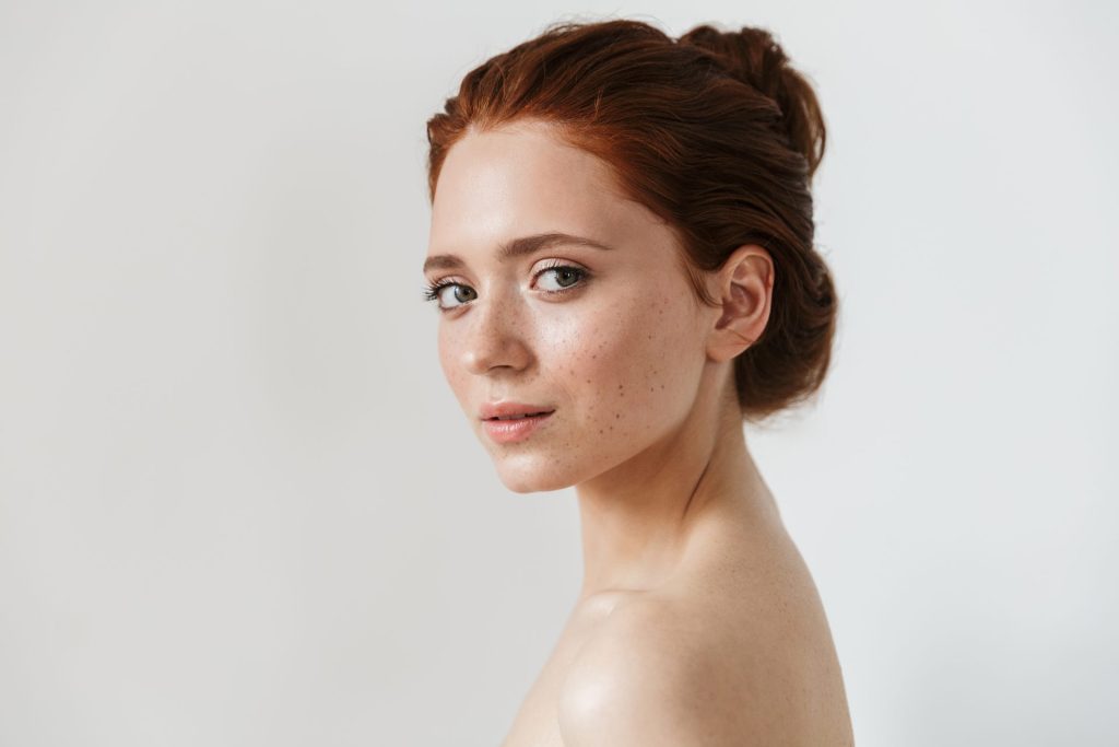 Redhead woman with clear skin and bare shoulders, for our post on foods and drinks that cause acne